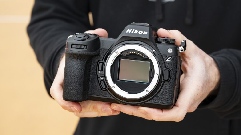 A person holds a Nikon Z camera, showcasing its lens mount and buttons against a blurred sandy background.