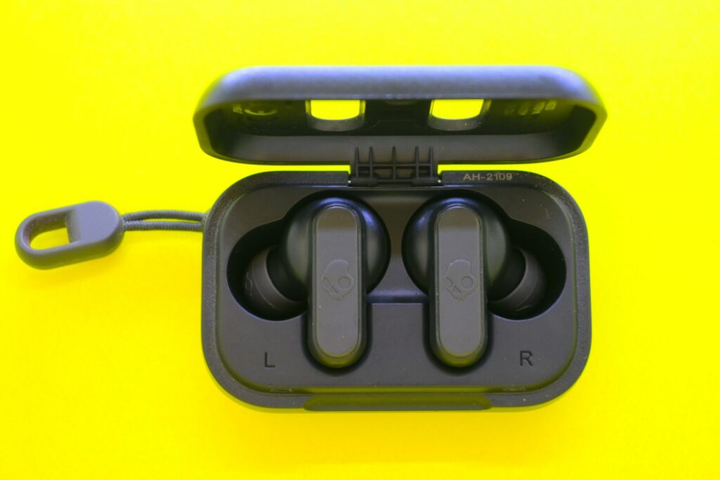 Black wireless earbuds resting in their case against a bright yellow background, displaying "L" and "R" indicators for left and right.