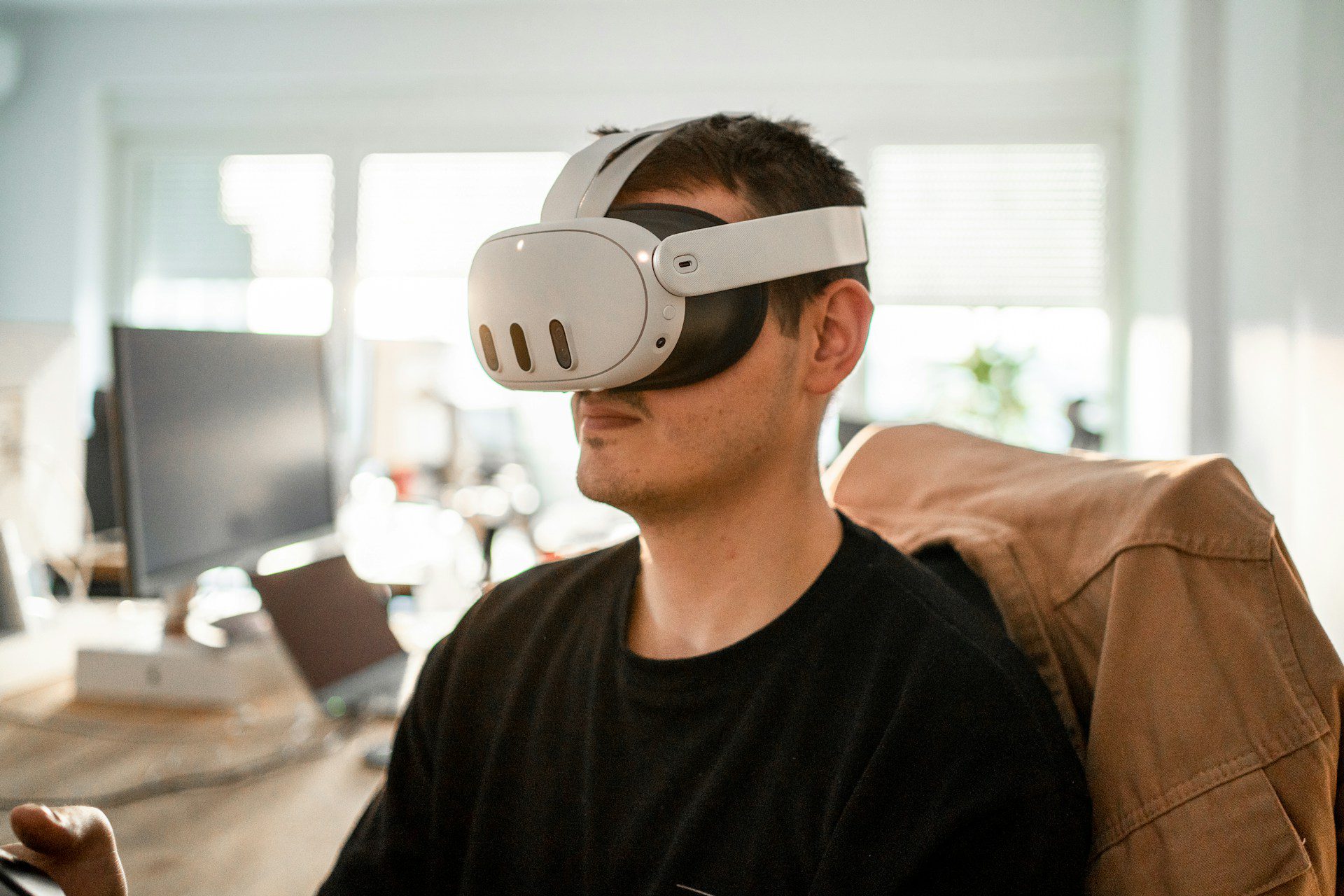 A person wearing a virtual reality headset sits in a modern office space, focused on an unseen screen.