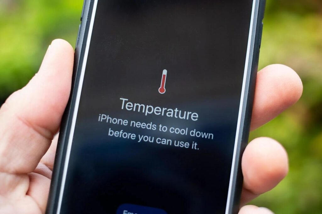 A hand holding a phone displaying a warning that the iPhone needs to cool down before use, with a thermometer icon.