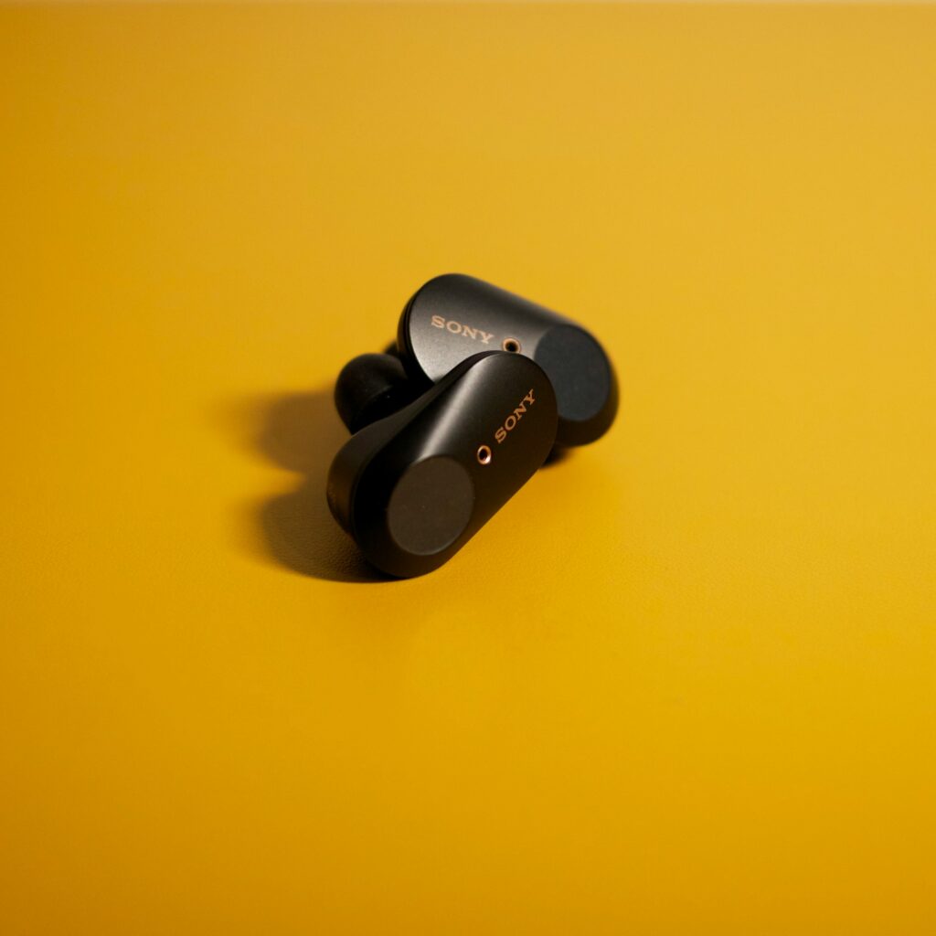 A pair of sleek Sony wireless earbuds rests on a vibrant yellow surface, showcasing their modern design and logo.