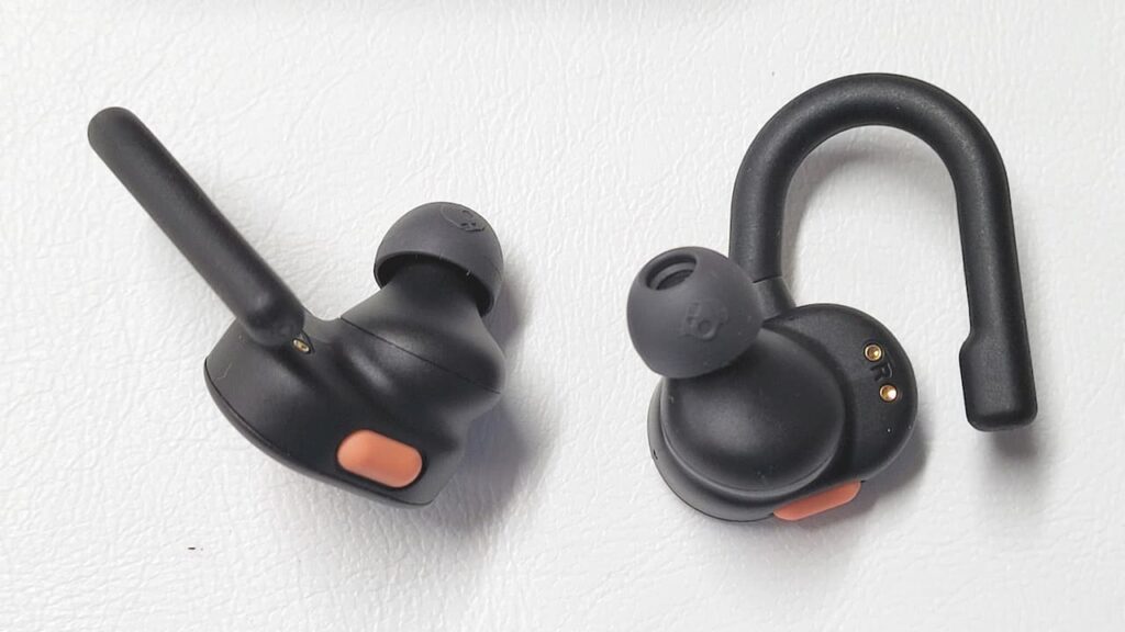 Two black wireless earbuds with an orange accent, one featuring a hook design for secure fit, on a white surface.