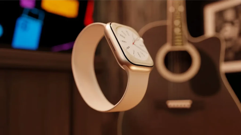 A gold Apple Watch with a light pink sport band is displayed against a warm, blurred background featuring a guitar and colorful lights. The watch face is analog, showcasing its sleek design and premium finish.