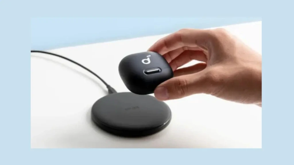 A hand holds a black charging case above a wireless charging pad, both positioned on a light surface.