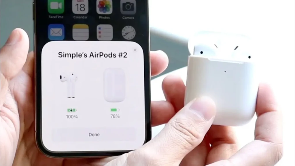 A person holds an iPhone in one hand and an open white AirPods case in the other. The iPhone screen displays a pop-up titled "Simple's AirPods #2," showing the battery levels for the earbuds (100%) and the case (78%), with a "Done" button at the bottom.
