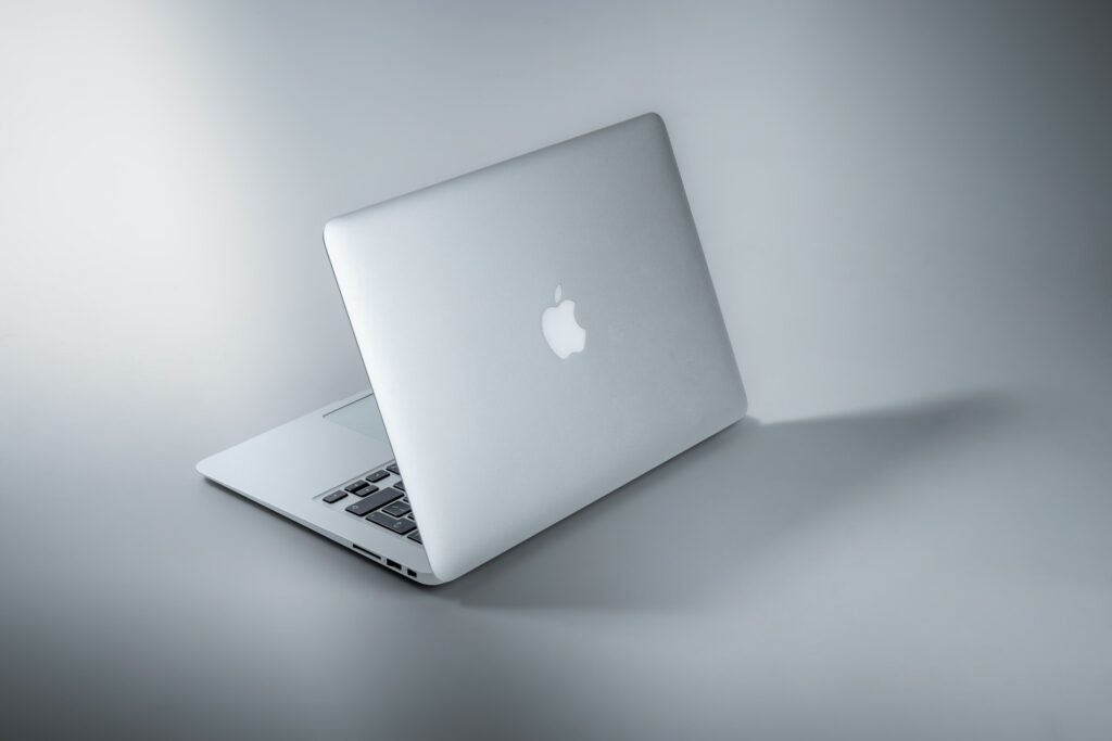 A sleek, silver Apple MacBook is positioned at an angle, showcasing its minimalist design and iconic logo against a light backdrop.
