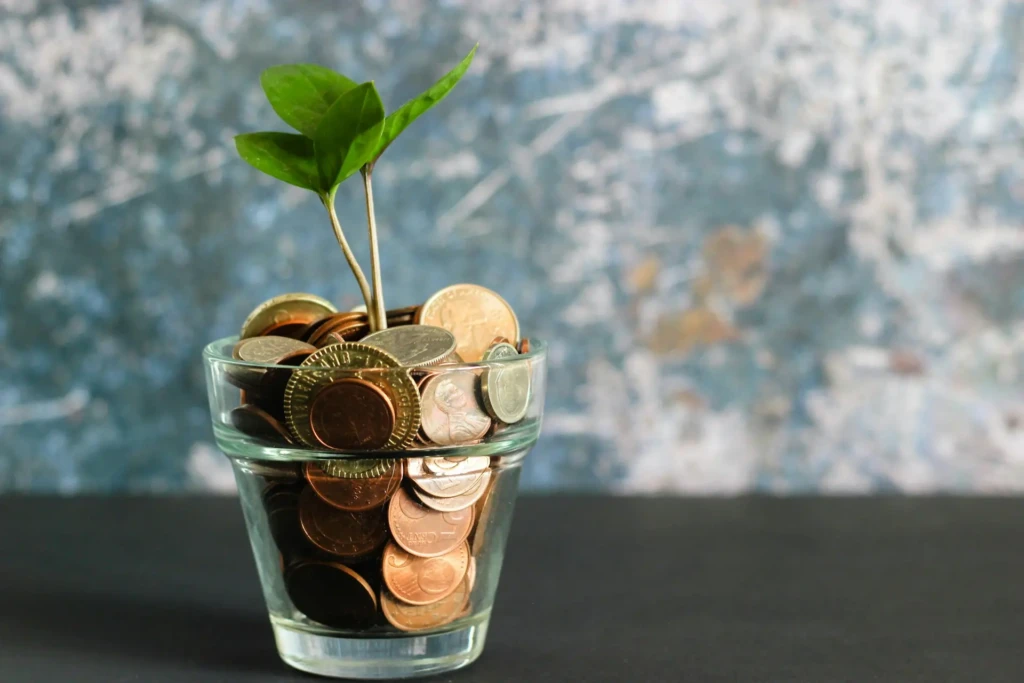 A glass jar filled with coins features a small green plant sprouting from the top, symbolizing growth and financial prosperity.