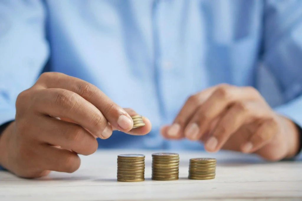 A person's hands are stacking coins on a table, organizing them into neat piles.