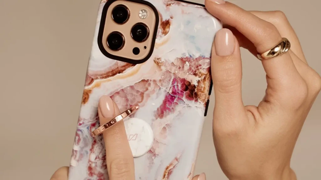 Close-up of a hand holding a smartphone with a pink and white marble-patterned case and a circular ring grip attached