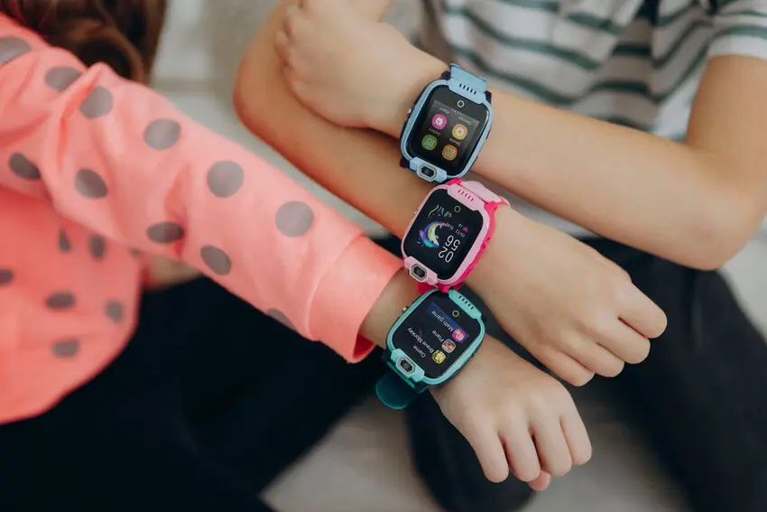Close-up of children’s arms wearing colorful kids smartwatches with app icons visible on the screens.
