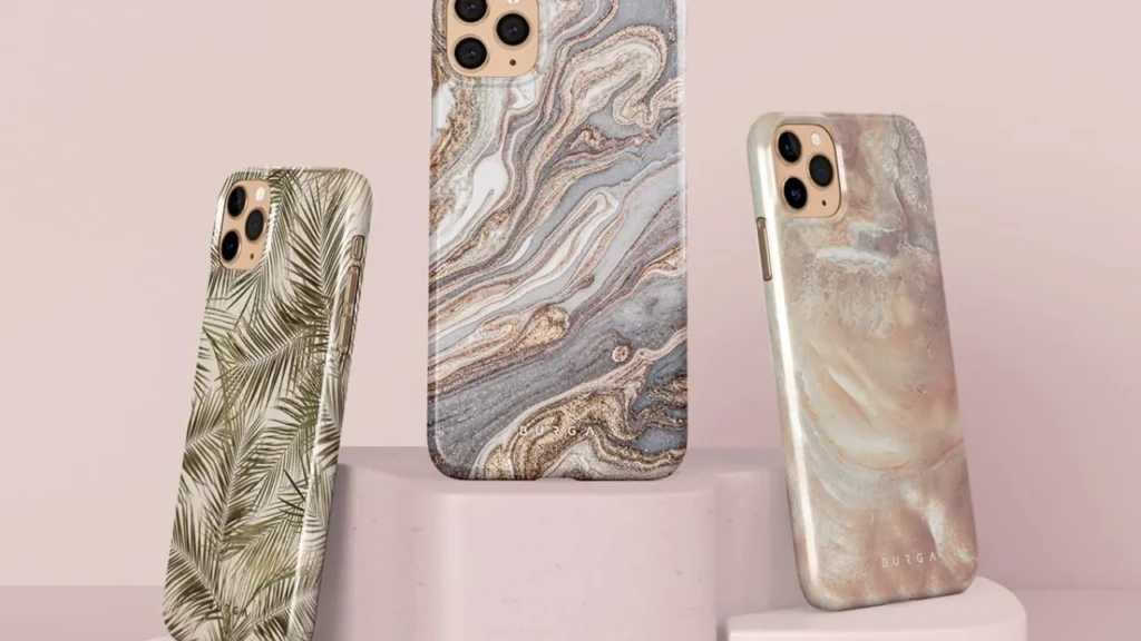 Three smartphones displayed upright on pedestals wearing marble and leaf-patterned protective cases against a neutral background