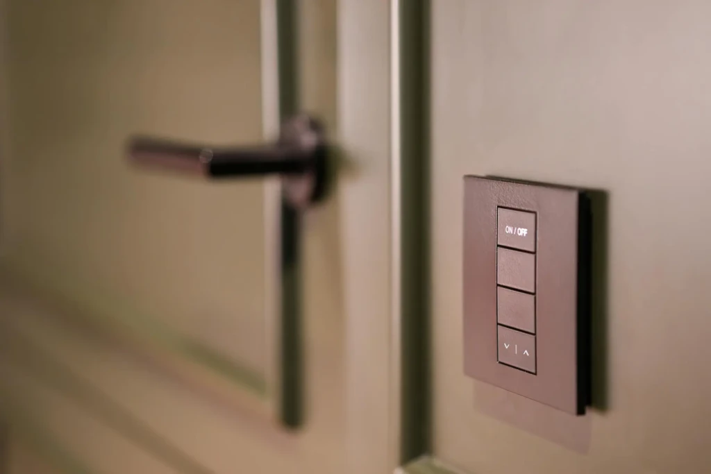 A close-up of a modern light switch panel with four buttons, mounted on a green wall next to a black door handle.