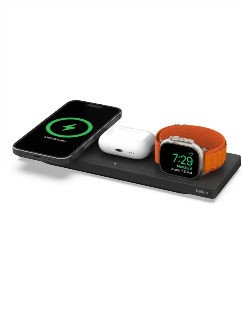 A Belkin multi-device wireless charging pad simultaneously powering an iPhone displaying “100% Charged,” a pair of AirPods, and an Apple Watch with an orange band, showcasing seamless compatibility and efficient charging for multiple Apple devices in one compact setup.