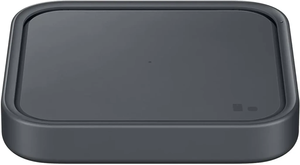 A close-up of a matte black Samsung wireless charging pad with a single circular charging zone and status indicator lights, emphasizing its compact, minimalist design ideal for desks or bedside tables for everyday device charging.