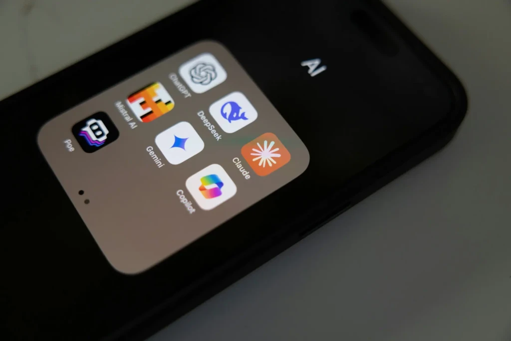 Smartphone screen displaying a folder of AI assistant apps including ChatGPT Gemini Claude Copilot DeepSeek Poe and Mistral arranged in a grid on a dark background