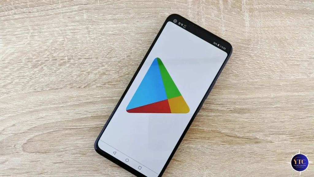 A black Android smartphone lying on a light wood surface, showing the Google Play logo on its bright white screen, highlighting its clean interface and seamless integration into everyday mobile use for app browsing and downloads.
