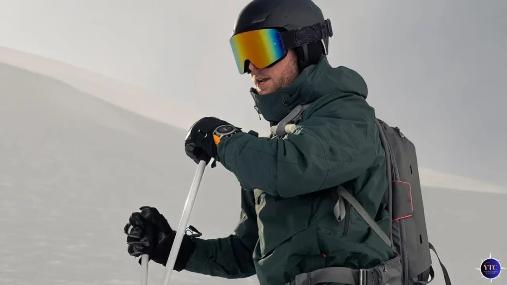 A skier in full gear, helmet, goggles, and winter jacket, glancing at his Garmin Fenix 8 on his wrist while standing on a snowy mountain slope. Emphasizes the watch’s rugged durability and performance in extreme winter sports conditions