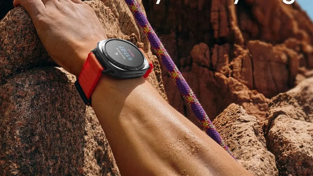 A person’s wrist wearing a Samsung Galaxy Watch Ultra with an orange strap, gripping a rock face during a climb. A purple climbing rope runs alongside, emphasizing the watch’s rugged design and outdoor fitness tracking capabilities