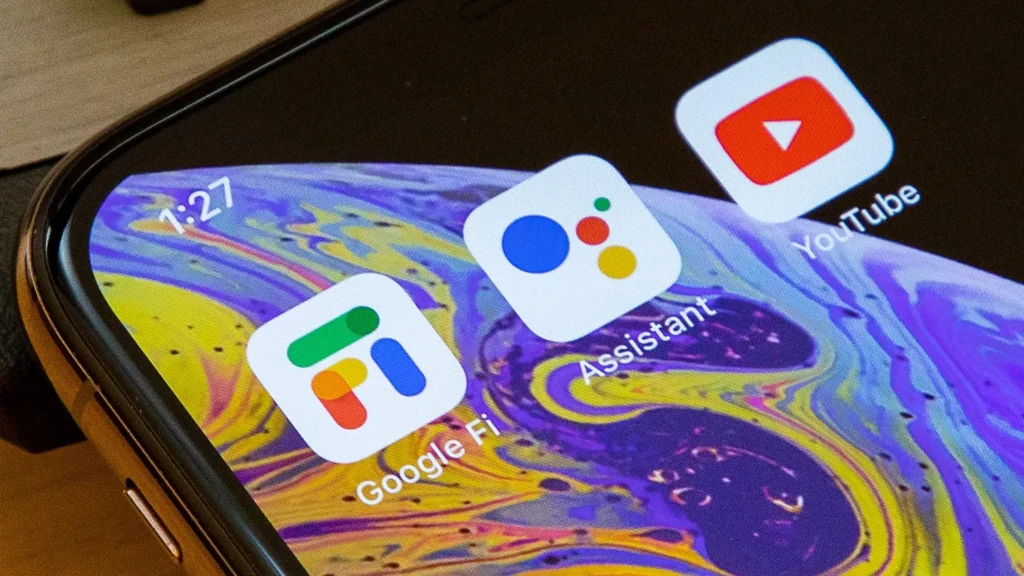 A close-up of a smartphone screen showing the Google Fi app icon alongside Google Assistant and YouTube icons on a colorful abstract wallpaper, emphasizing its role as a core Google service within the Android ecosystem for communication and connectivity.