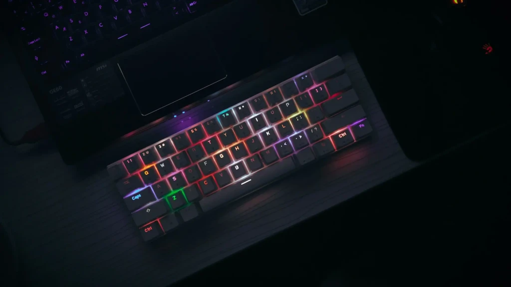 A close-up overhead view of an MSI laptop’s RGB keyboard glowing with rainbow lighting in a dark room, revealing model details like “GE60” and “Killer Networking” near the touchpad, emphasizing its premium build and immersive gaming atmosphere.