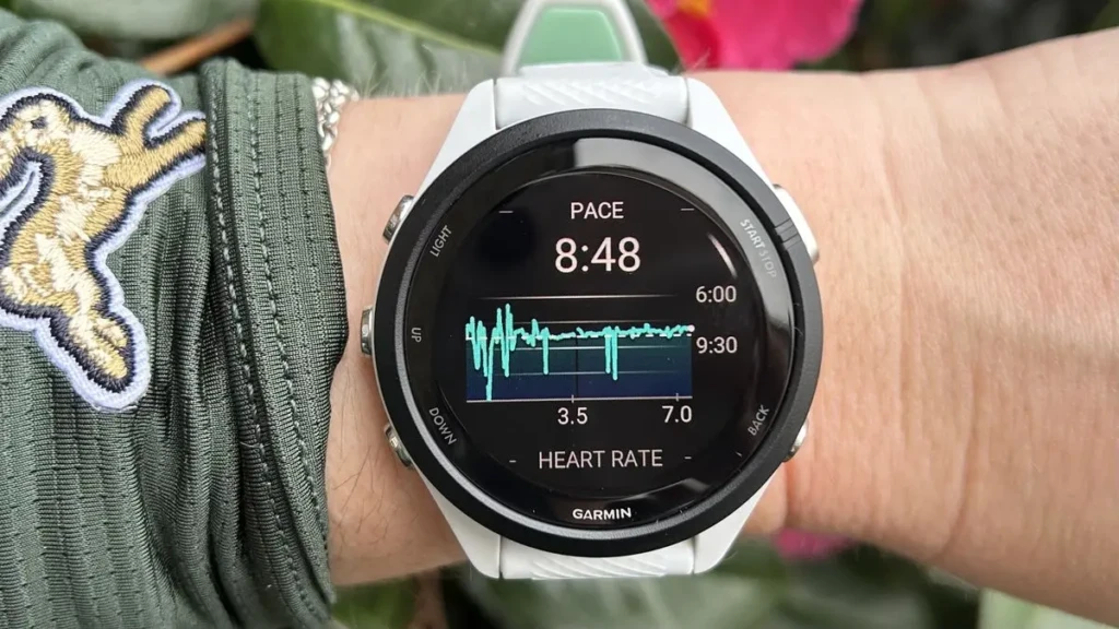 A person’s wrist wearing a white Garmin smartwatch during an outdoor run, displaying real-time running metrics: pace (8:48 min/mile) and heart rate graph. The sleeve features a rabbit patch, adding personality to the athletic scene, highlighting precision tracking in everyday activity