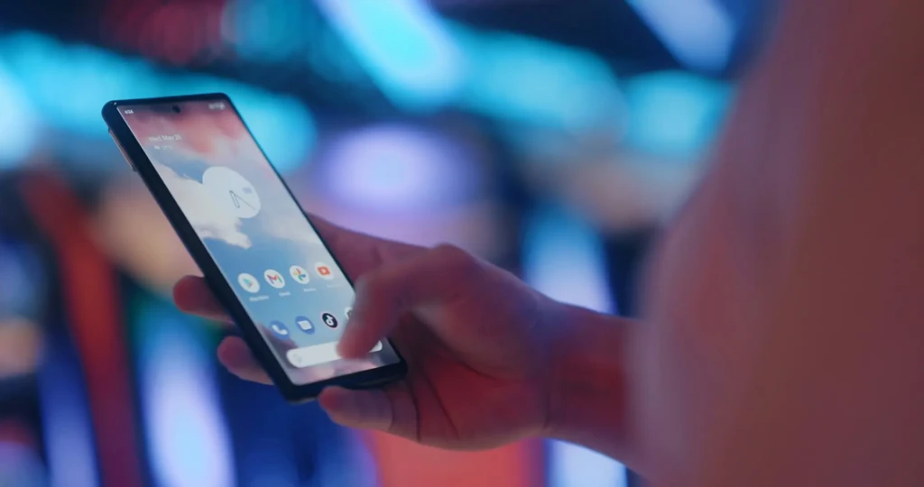 A hand holding a smartphone displaying the Android home screen with the Google Fi app icon visible, set against a vibrant, blurred city nightlife backdrop, illustrating real-world usage and seamless integration into daily mobile routines.