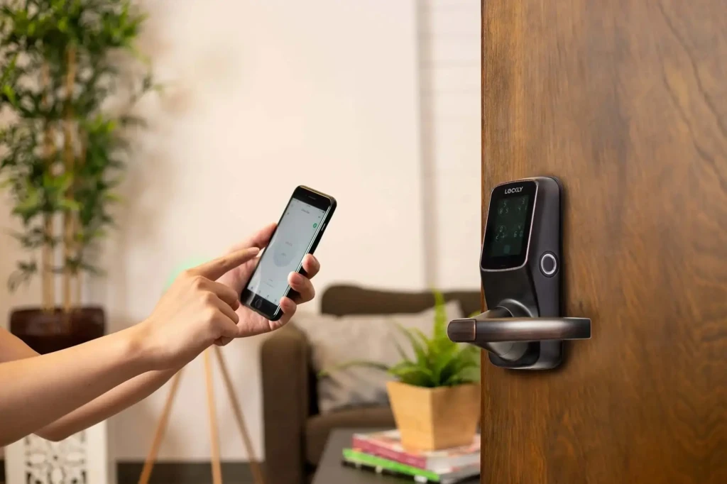 A person using a smartphone app to control a Lockly smart lock installed on a wooden door, set in a cozy living room with plants and books, demonstrating seamless remote access and smart home integration for everyday convenience.