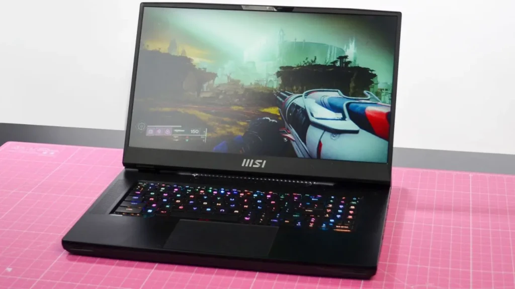A black MSI gaming laptop displaying an immersive first-person shooter game on its screen, with a vibrant RGB backlit keyboard glowing in multiple colors, placed on a pink grid mat against a white background, highlighting its high-performance visuals and customizable lighting.