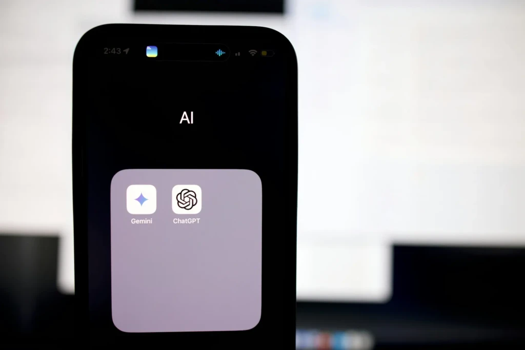 A close-up of an iPhone screen displaying a folder labeled “AI” containing app icons for Gemini and ChatGPT, illustrating how users organize and access popular AI tools directly from their mobile home screen.