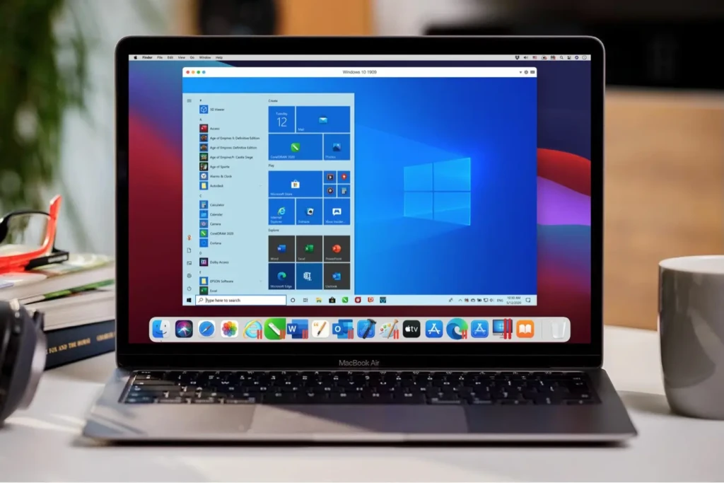 A MacBook Air running Windows 10 1909 inside a virtual machine window, with the macOS dock visible at the bottom and books, headphones, and a coffee mug arranged around the laptop, showcasing real-world usage of Windows apps on a Mac for productivity or gaming without rebooting.