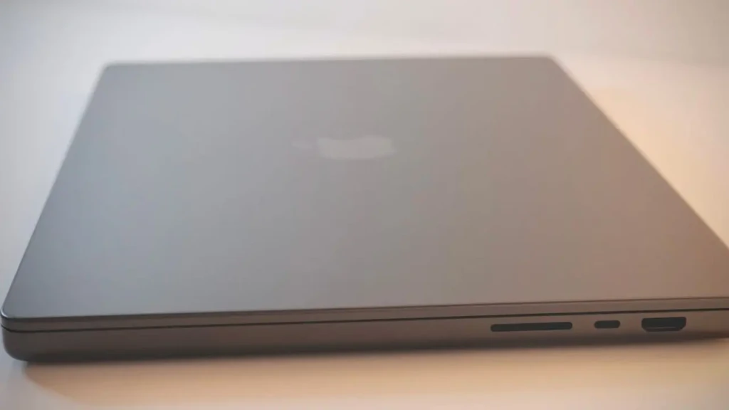A sleek, closed laptop with an Apple logo on top, showing side ports on a light background.