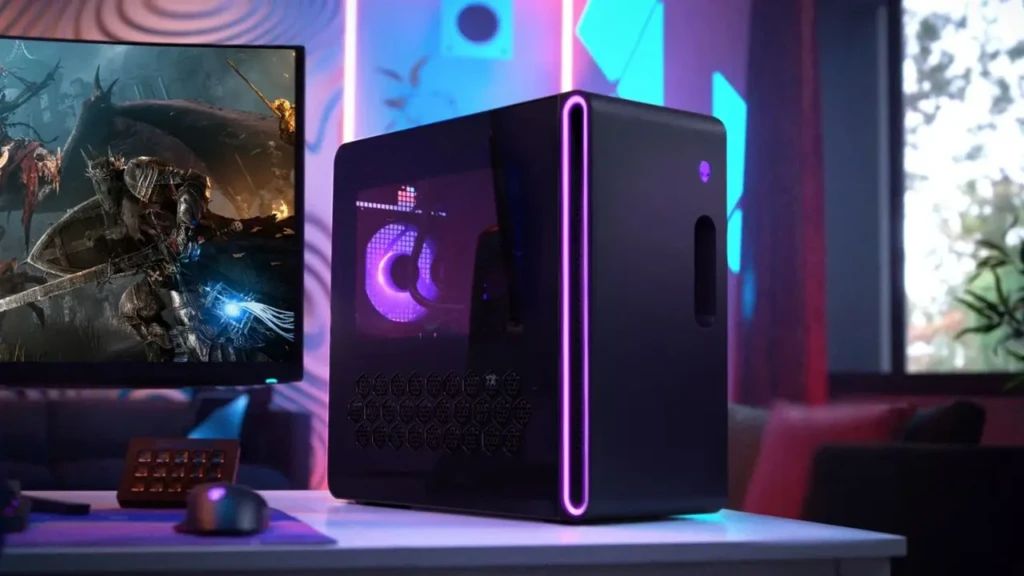 A compact black Alienware desktop PC with purple RGB lighting along its side and front vent, placed on a desk beside a monitor displaying a fantasy game, a keyboard, and a mouse, set in a vibrant, neon-lit gaming room with ambient blue and pink lighting.
