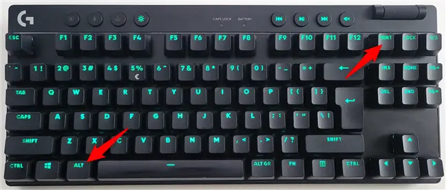 A backlit Logitech gaming keyboard with green illumination, showing two red arrows pointing to the Windows key (bottom-left) and the F12 key (top-right), suggesting a custom or manufacturer-specific screenshot shortcut, likely for Lenovo/Logitech hybrid setups or third-party software integration.