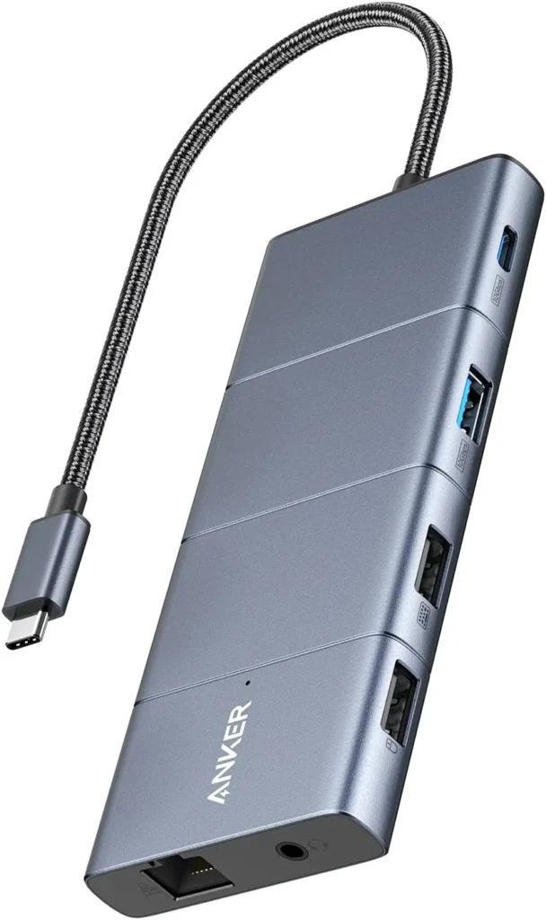 A gray Anker USB-C hub with a braided cable, displaying ports including USB-C (input), USB-A (blue), HDMI, Ethernet, and 3.5mm audio jack, with the “ANKER” logo engraved on the side, illustrating a portable, travel-friendly expansion solution.