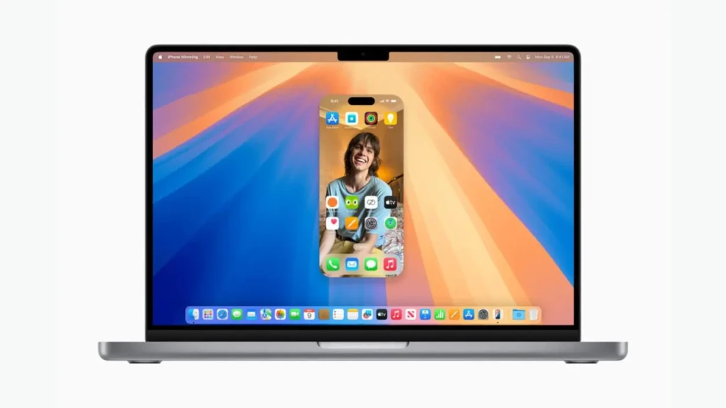 A MacBook displaying the iPhone Mirroring feature, with a live iPhone home screen (showing a smiling person and app icons) overlaid on the Mac’s vibrant orange-and-blue desktop wallpaper, illustrating seamless cross-device continuity in macOS Sequoia.