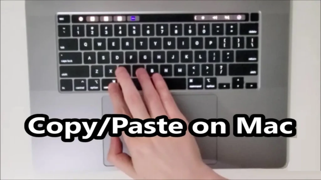 A top-down view of a hand using the trackpad while the text “Copy/Paste on Mac” is overlaid; the MacBook’s keyboard and Touch Bar are visible, illustrating gesture-based or hybrid interaction during clipboard tasks.