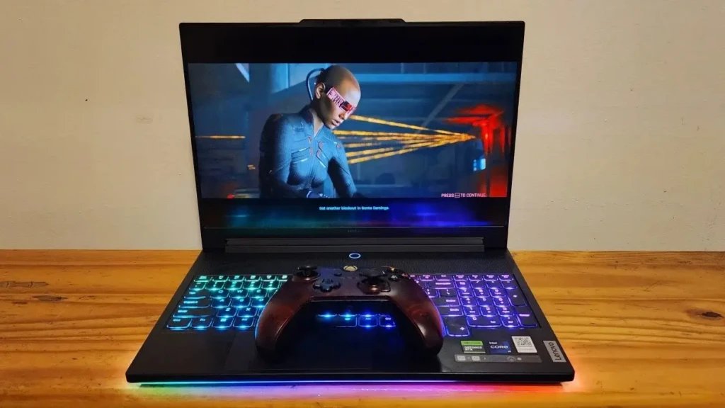 A gaming laptop displays a vibrant scene while an Xbox controller sits in front, illuminated by colorful keyboard backlighting.