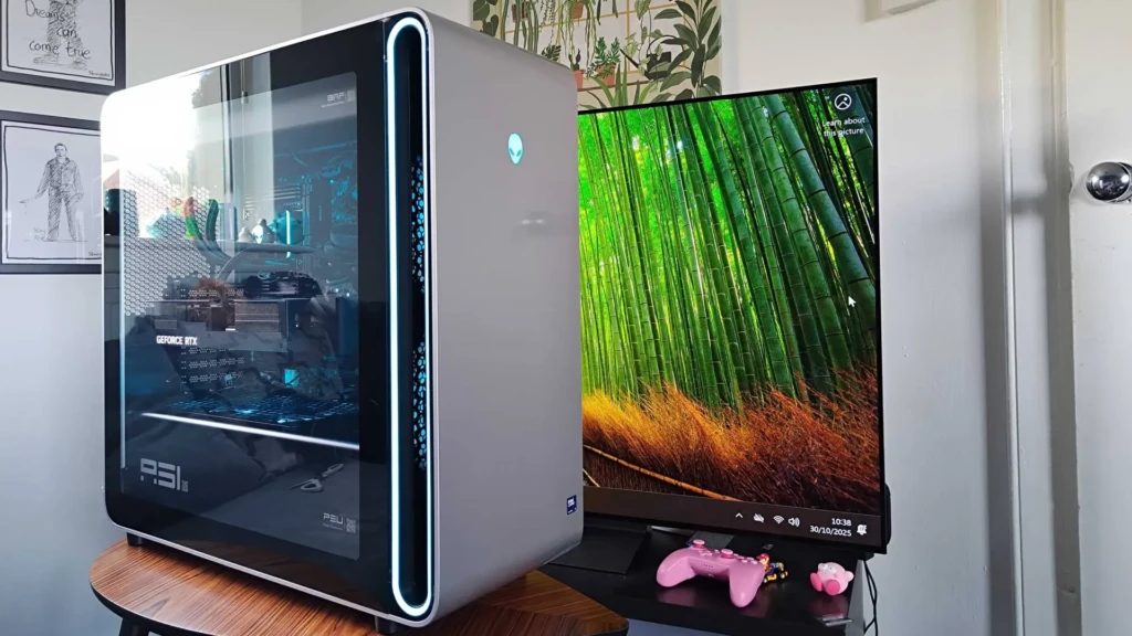 A sleek gaming PC with a transparent side panel showcases an RTX graphics card, next to a large display featuring bamboo scenery. A pink controller rests below.
