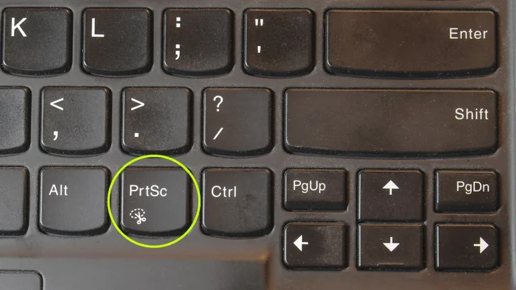 A close-up of a black laptop keyboard with the “PrtSc” (Print Screen) key circled in green and labeled with a scissors icon, emphasizing the traditional full-screen capture method on Windows laptops.