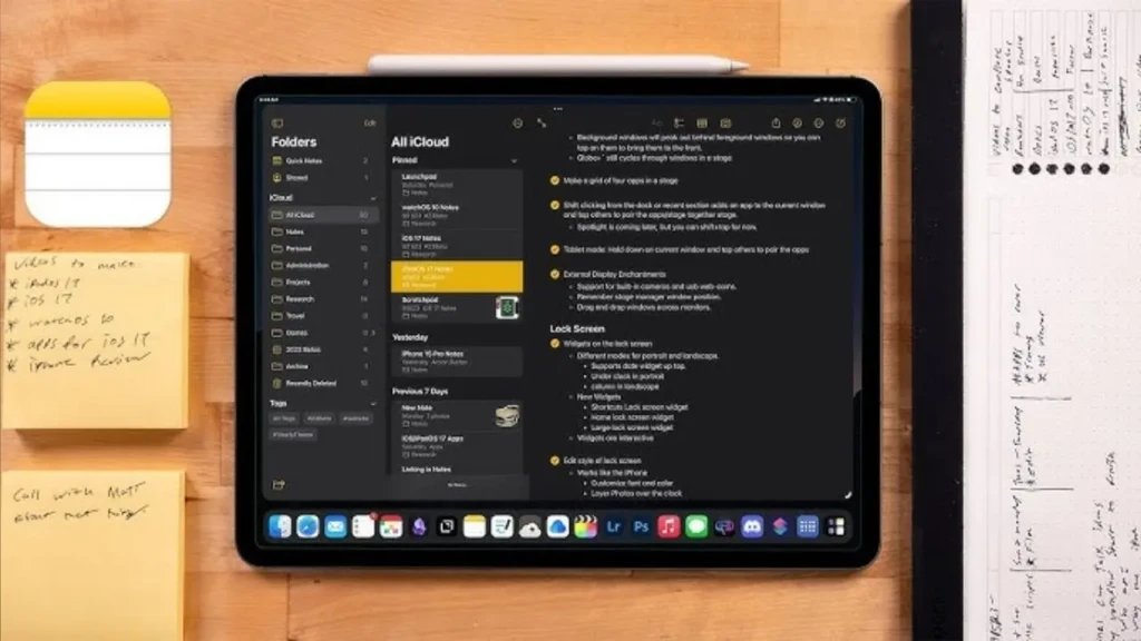 An iPad displaying the Notes app in dark mode, with a detailed note titled “All iCloud” open, showing rich text formatting, bullet points, and folder organization; a white Apple Pencil rests on top, and physical sticky notes and a notepad surround the device, highlighting productivity, handwriting support, and ecosystem integration.