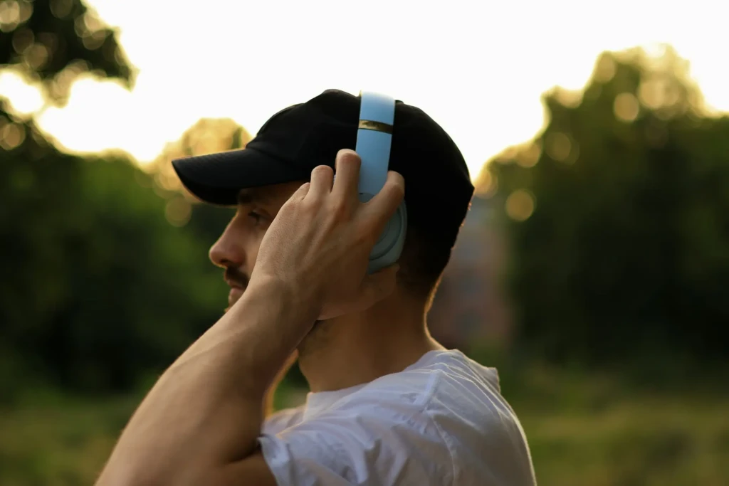 A man wearing headphones sits on a bench in a park, enjoying the outdoors and listening to music.