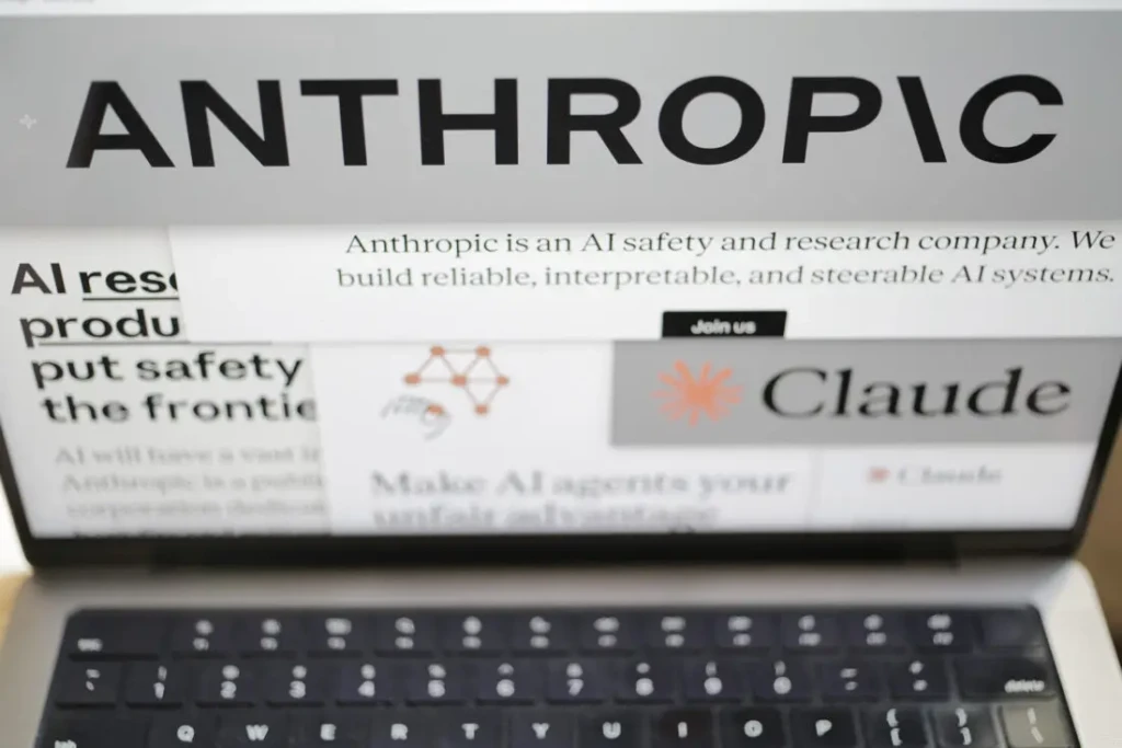 A close-up of a laptop screen displaying Anthropic’s website, with the bold “ANTHROPIC” header visible above text stating “Anthropic is an AI safety and research company. We build reliable, interpretable, and steerable AI systems,” alongside partial views of the Claude logo, “Join us” button, and AI-related slogans, illustrating the company’s mission and branding in a real-world usage context.
