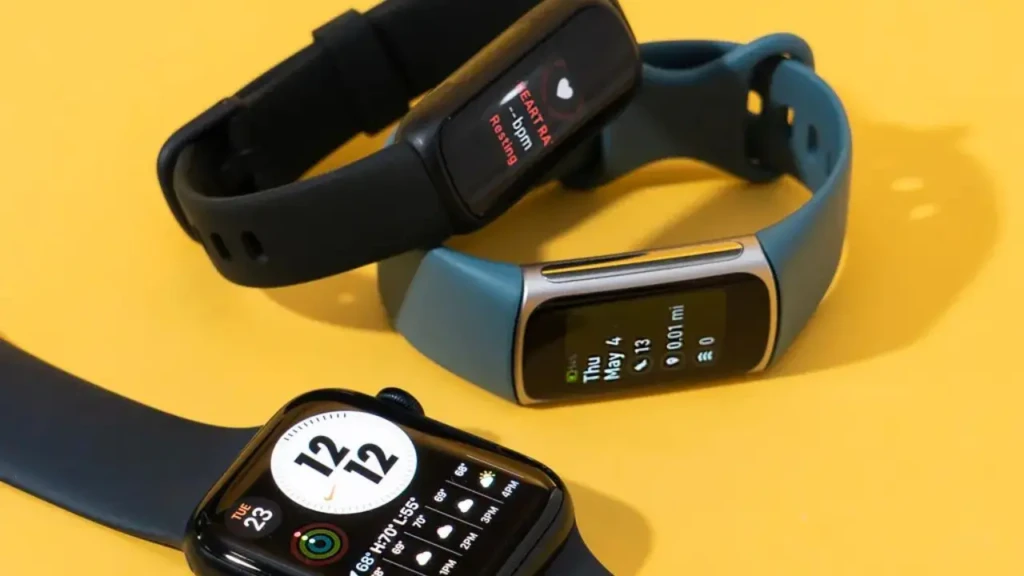 Three fitness trackers on a yellow background: a black Fitbit-style band showing “HEART RATE, bpm Resting,” a teal band displaying date and distance (“Thu May 4, 0.01 mi”), and an Apple Watch with analog watch face and complications, highlighting diverse form factors and health-tracking capabilities.