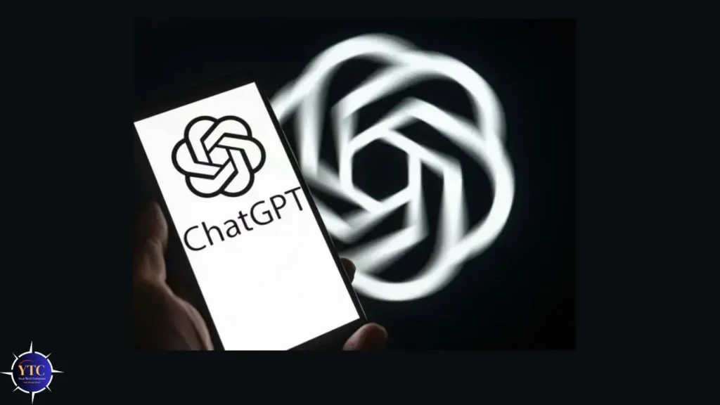 A hand holding a smartphone showing the ChatGPT logo (interlocking rings) and text on a white screen, with a large glowing ChatGPT symbol projected softly in the background, emphasizing OpenAI’s conversational AI interface and visual identity.