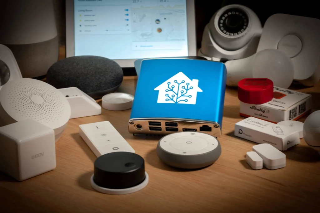 A diverse collection of smart home devices on a desk, including hubs, sensors, cameras, bulbs, and branded accessories (e.g., Shelly, Phoscon, Aeotec), centered around a blue tablet displaying a networked house icon, symbolizing ecosystem integration and IoT interoperability.