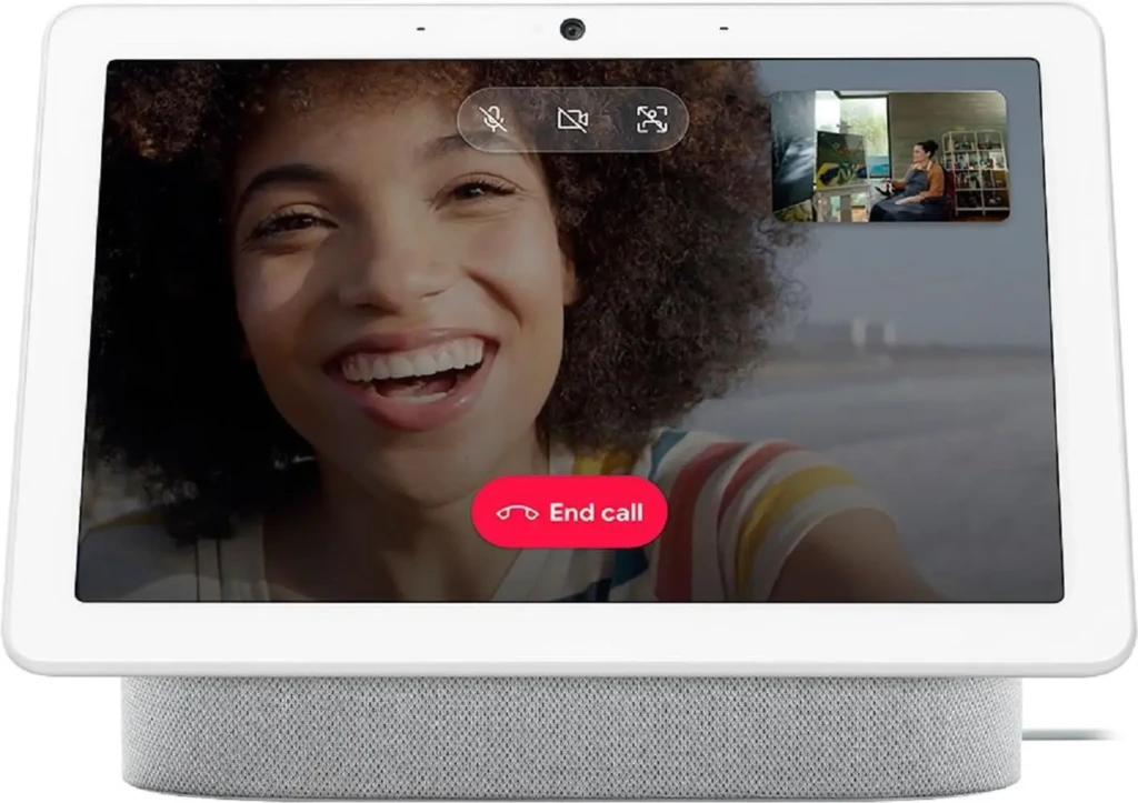 A Google Nest Hub (2nd gen) showing a video call in progress: a smiling woman in the main view and a smaller picture-in-picture of the remote participant, with on-screen controls for mute, camera, and a prominent red “End call” button, demonstrating hands-free communication and smart display functionality.