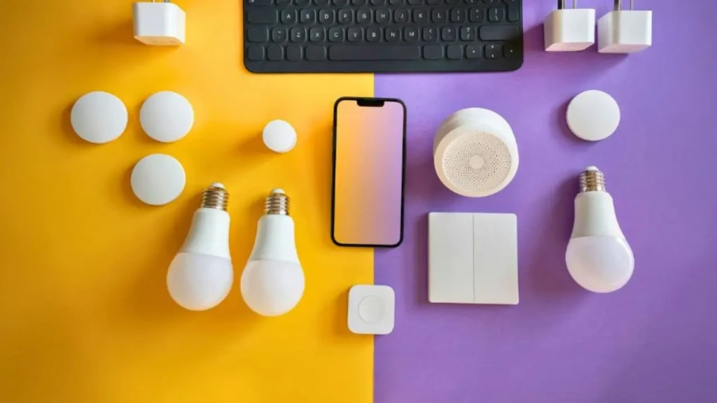 A flat-lay composition split diagonally between yellow and purple backgrounds, showcasing smart bulbs, sensors, switches, a smartphone, and a keyboard, highlighting product variety, design cohesion, and the blend of hardware and mobile control in smart home setups.