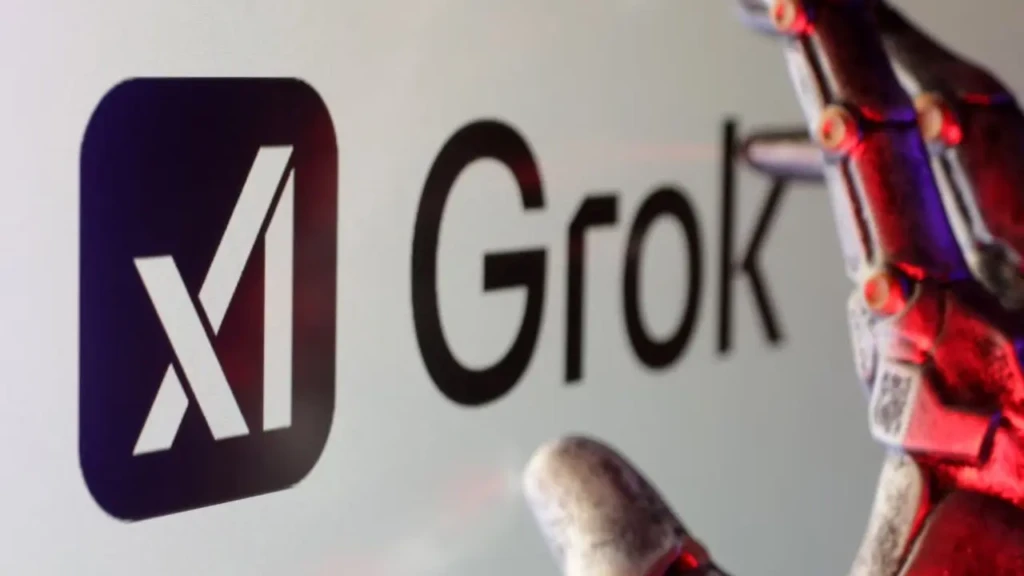 A close-up of the xAI Grok logo (white “x” in a dark square beside “Grok” text) on a screen, with a metallic robotic hand partially visible in the foreground under red-and-blue lighting, symbolizing human–AI collaboration and advanced AI integration.