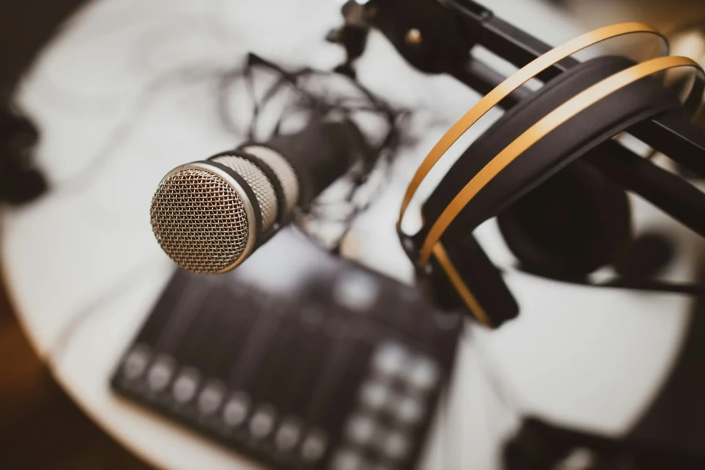 Close-up of a professional microphone and headphones on a stand, with a blurred audio mixer in the background, creating a focused and creative atmosphere.