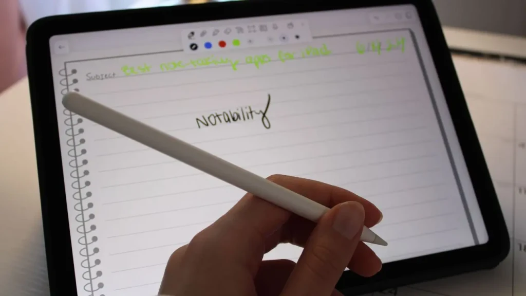 A hand holds a stylus above an iPad displaying a digital notebook. The screen shows handwritten notes about a note-taking app called "Notability."